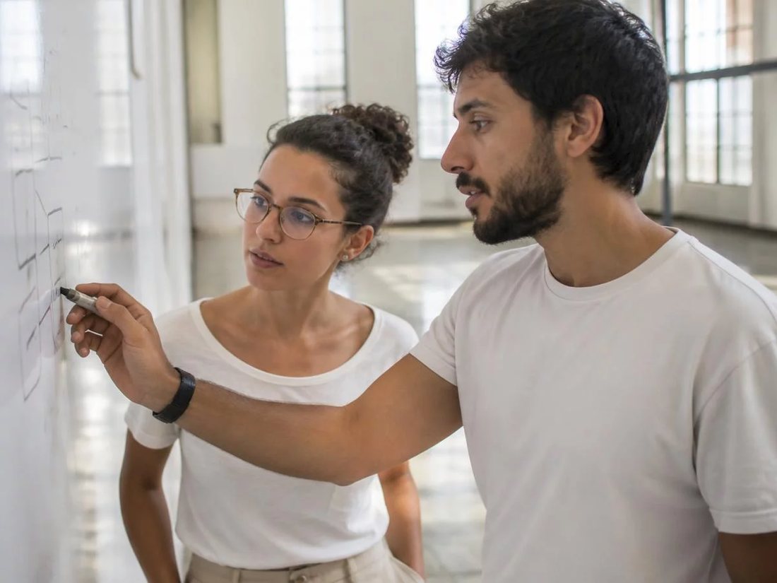 Duas pessoas diante do quadro branco com a armação de um argumento rabiscada